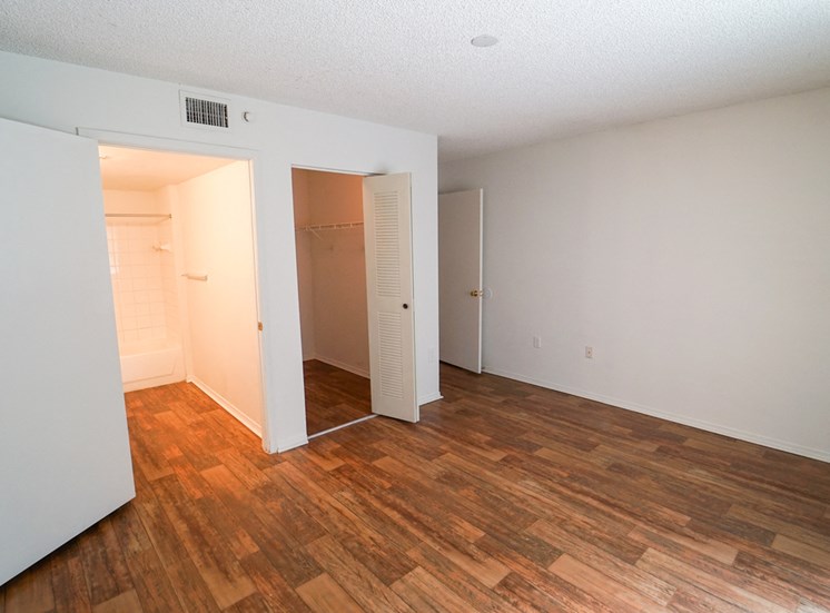 Bedroom with Hardwood Style Flooring and Open Empty Closet Next to En Suite Bathroom