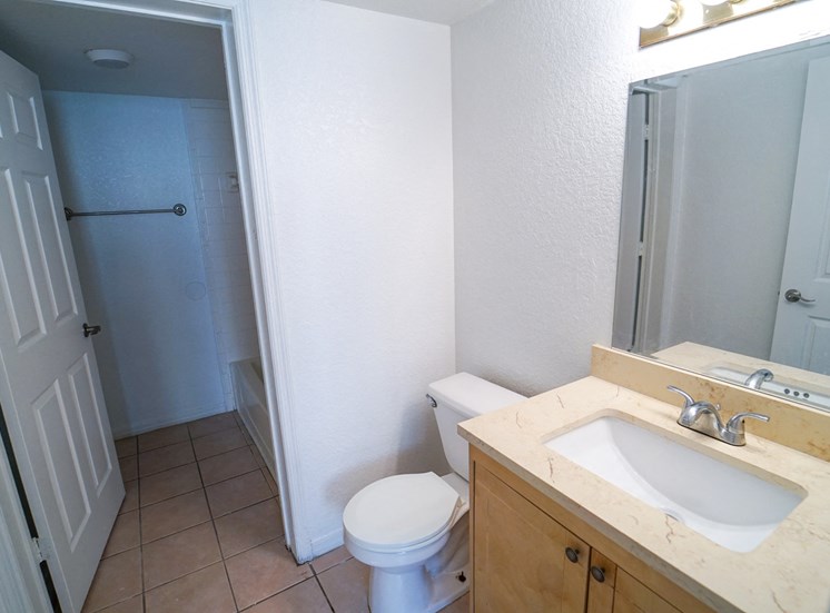 Bathroom with Tan Counters  and Wood Cabinets Next to Toilet and Separate Room with Bathtub