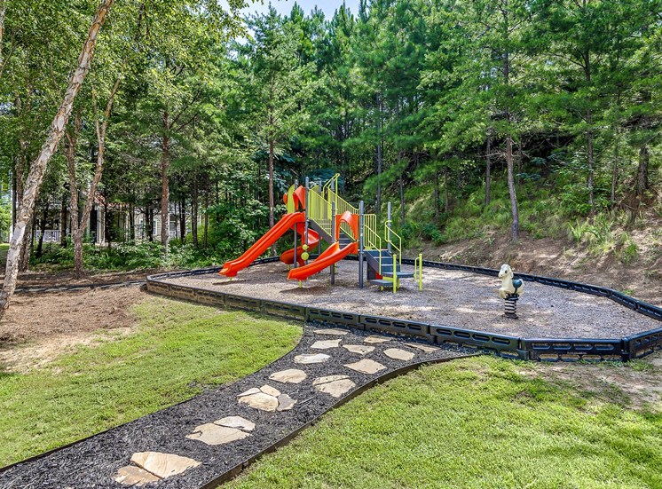 Playground jungle gym and playground slides in a bed of mulch with trees, and swings in the background