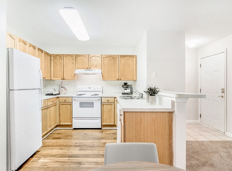 Kitchen with white appliances and brown cabinets. Coffee maker and dishes on countertop.