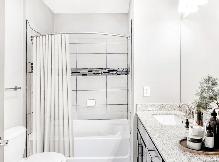 Staged Bathroom with tile floors, toilet, shower/tub combo and dark cabinets. Towles, lotions used as décor, and shower curtain.