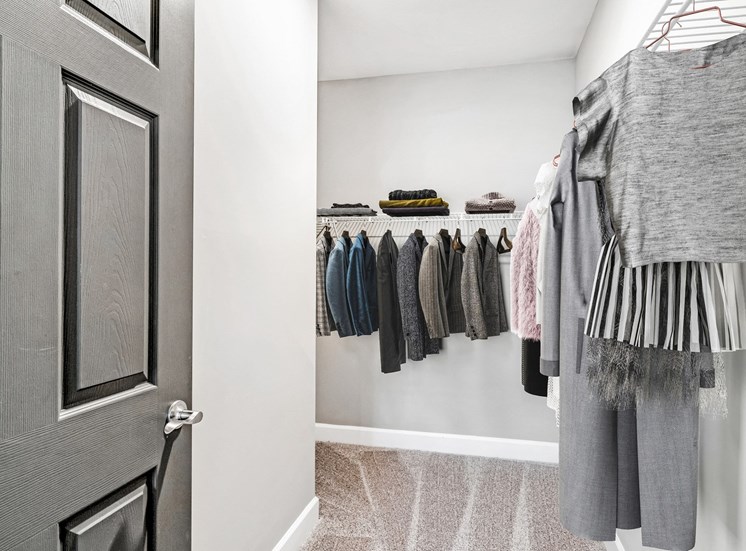 Spacious carpeted closet with mounted metal shelves filled with hanging clothes