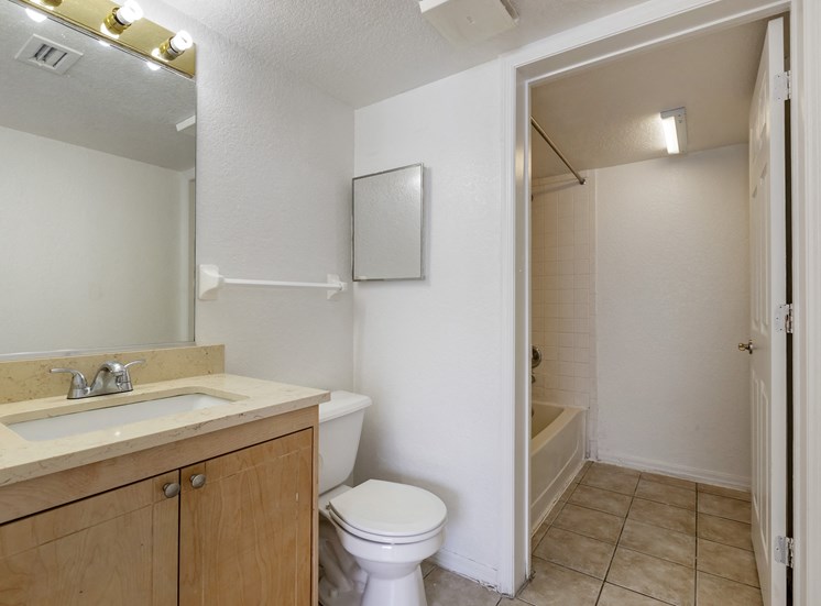 Bathroom with Tan Counters and Wood Cabinets Next to Toilet and Separate Room with Bathtub