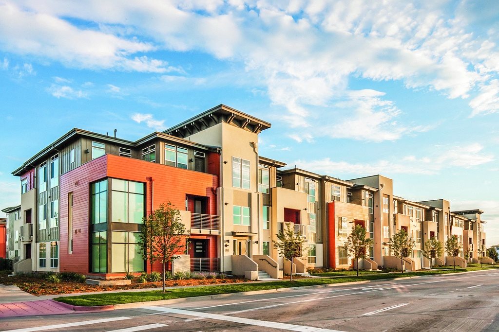 Apartment Building Exterior Against Blue Sky with Roadway and Sidewalk with Trees Lining it