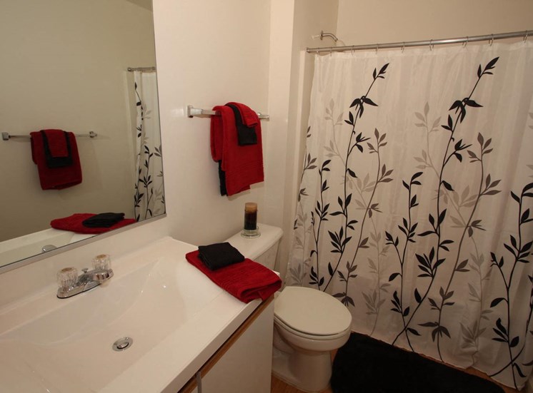 Bathroom with shower curtain and sink with white counter top and red towels hung up
