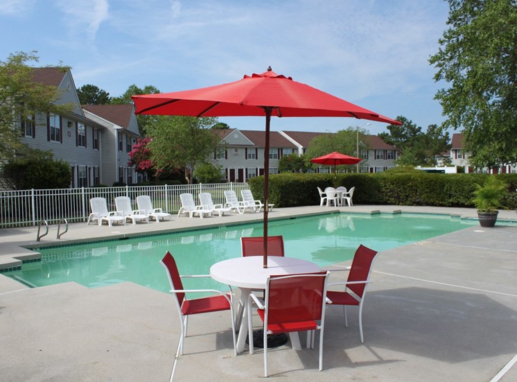 Community swimming pool with four red chairs and a red umbrella surrounding a table