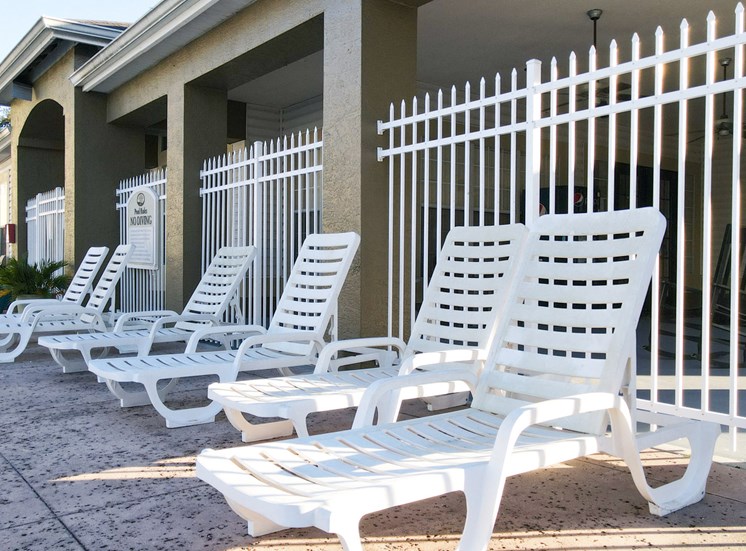 White pool lounge chairs on sun deck surrounded by white metal fence