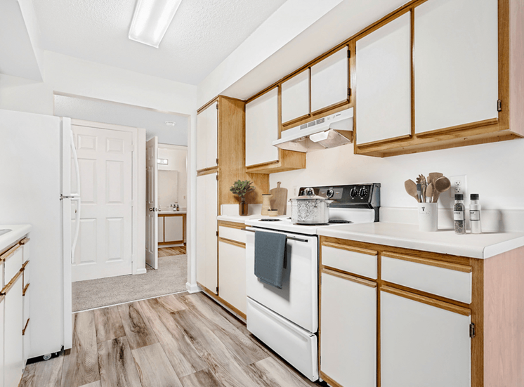 Virtually staged; Kitchen with wood floors, white appliances, and wood cabinets. Guest bathroom in background. Kitchen accessories displayed