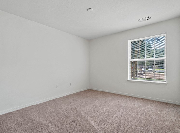The vacant second bedroom features wall-to-wall beige carpet, white walls, and a large window on the back right wall. To the right is the doorway to the bedroom closet.