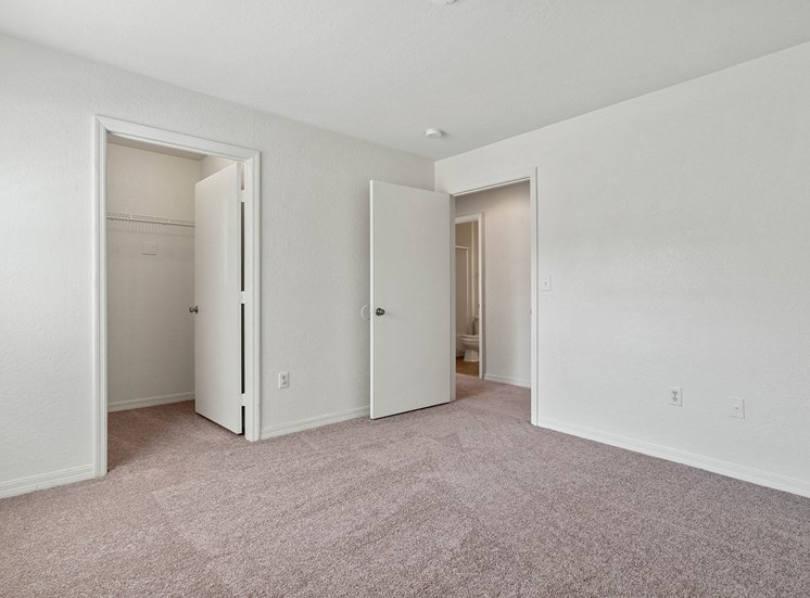 The secondary bedroom has white walls and light beige carpet. There is a closet to the left with a white wire shelf. The bedroom door opens inward to the main hallway adjacent to the hall bathroom.