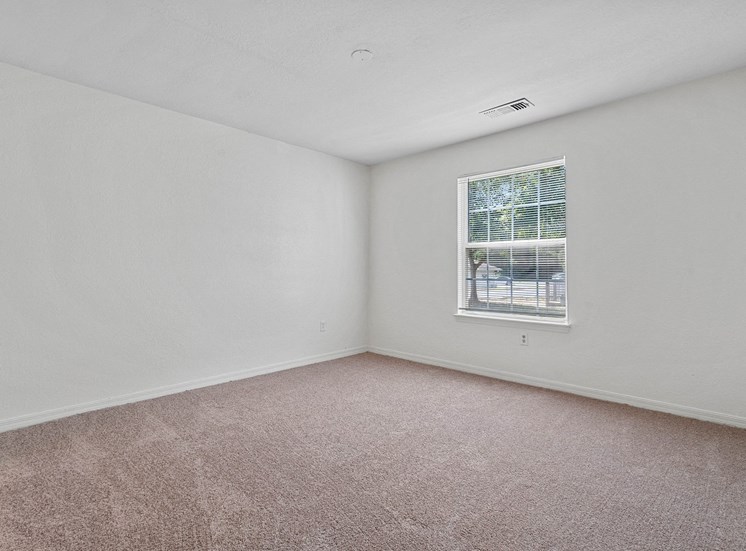 The third bedroom has white walls, white ceiling, and wall to wall beige carpet. Opposite the doorway is a standard window with blinds on the far right wall.