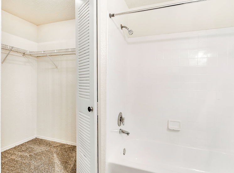 Carpeted walk in closet inside of the bathroom next to the tub with white tile and chrome finishes