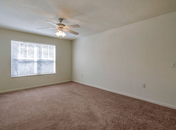 Spacious living room with carpet flooring, multi speed ceiling fan, and large window for natural lighting