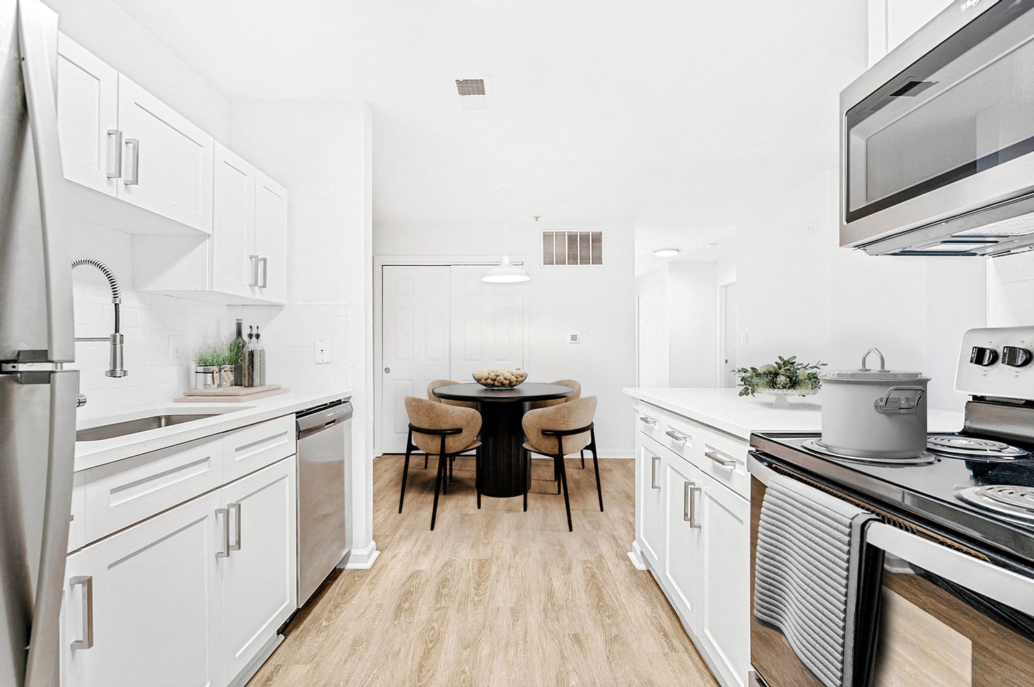 White cabinets, white subway tile back splash and stainless-steel appliances can be seen in the upgraded kitchen. View of dining room with coat closet with sliding doors in the background
