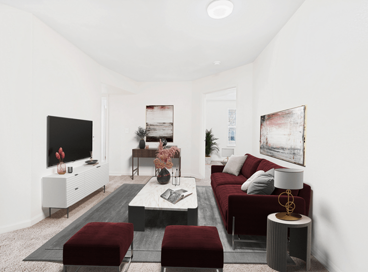 Virtually staged carpeted living room with maroon couch and accent chairs with coffee table and modern artwork. Bedroom in background