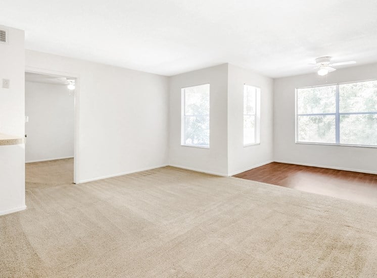 Vacant living with carpet, a study with hardwood-style flooring, a ceiling fan, and several windows with window blinds.