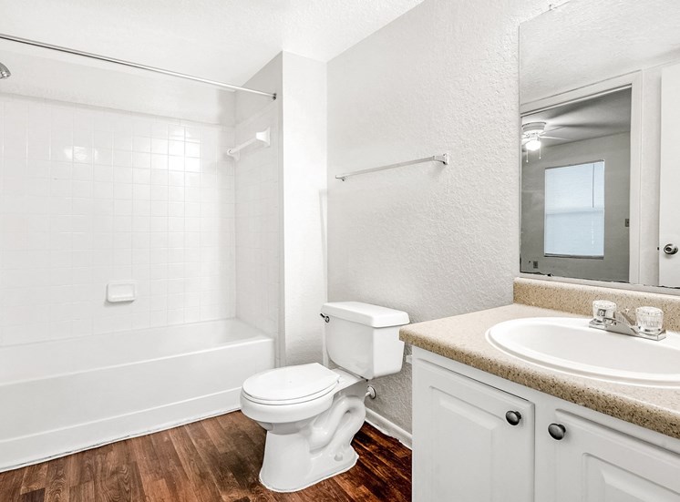 Vacant bathroom with hardwood-style floors, a shower/tub combo with tile surround, a single sink vanity with laminate countertops, and white cabinets.