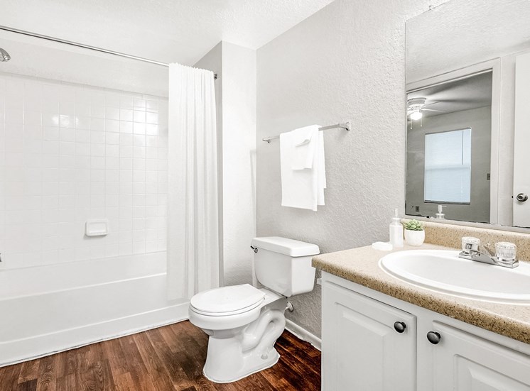 Staged bathroom with hardwood-style floors, a shower/tub combo with tile surround, a single sink vanity with laminate countertops, and white cabinets.