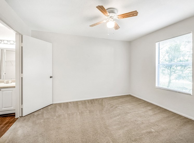 A vacant bedroom with carpet, a ceiling fan, window, and an en suite bathroom.