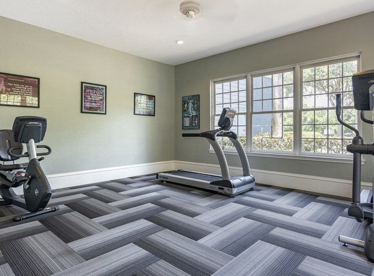 Fitness center with cardio equipment and large windows for natural lighting