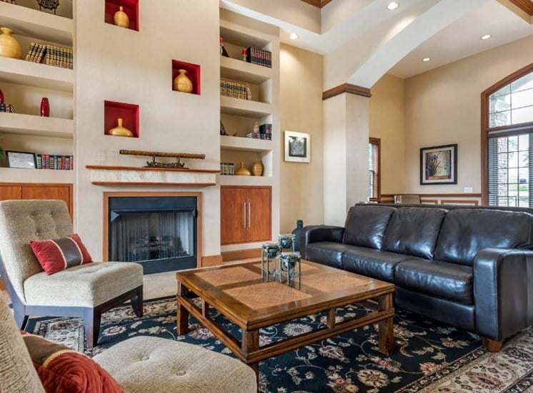 Clubhouse lounge with couches, chairs, coffee table, rug, fire place, and book shelves