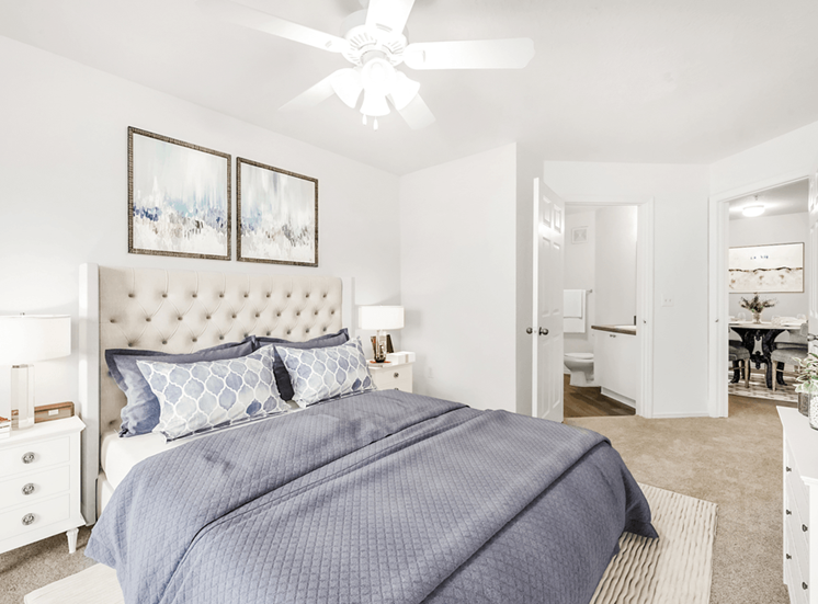 Virtually staged bedroom with carpet, white walls, accent run, ceiling fan with light, white dresser and nightstands with lamps and wall decor
