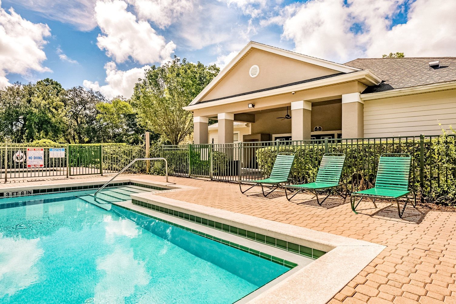 Swimming pool with a brick paver sundeck and lounge chairs outside the clubhouse.