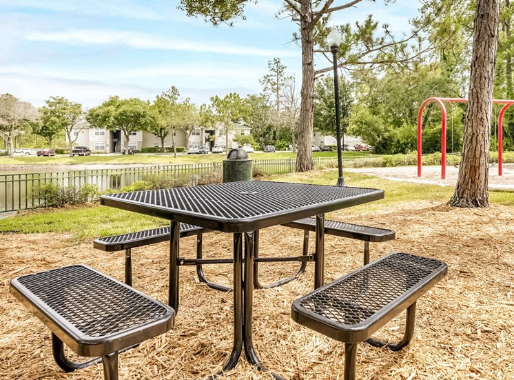 Table with four bench seats near the playground and swing sets.