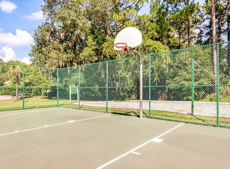 A fenced-in basketball court adjacent to a sand volleyball court.