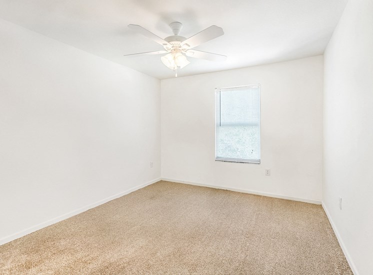 Vacant bedroom with carpet, a window, and a ceiling fan.