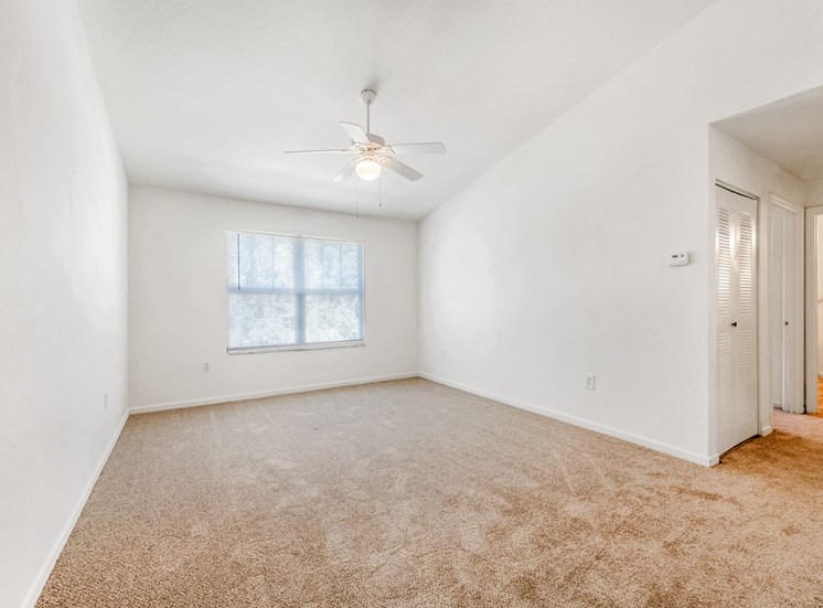 Vacant living room with carpet, a ceiling fan, and a window.