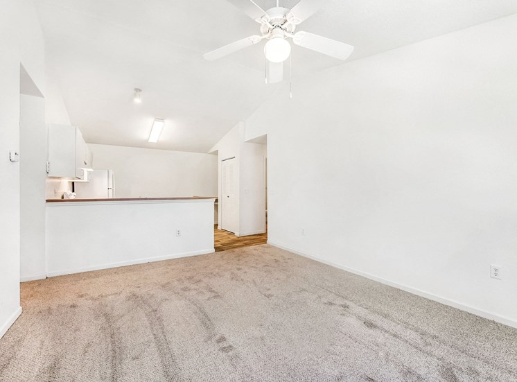 Vacant living room and kitchen with a breakfast bar, carpet, and a ceiling fan.