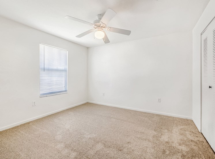 Vacant bedroom with carpet, a ceiling fan, a window, and a closet.