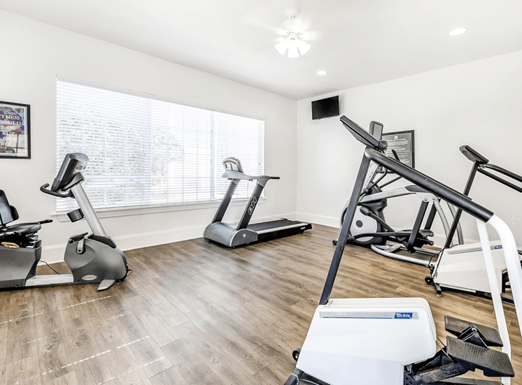 Fitness center with cardio machines and large window with wall mounted television and ceiling fan with light
