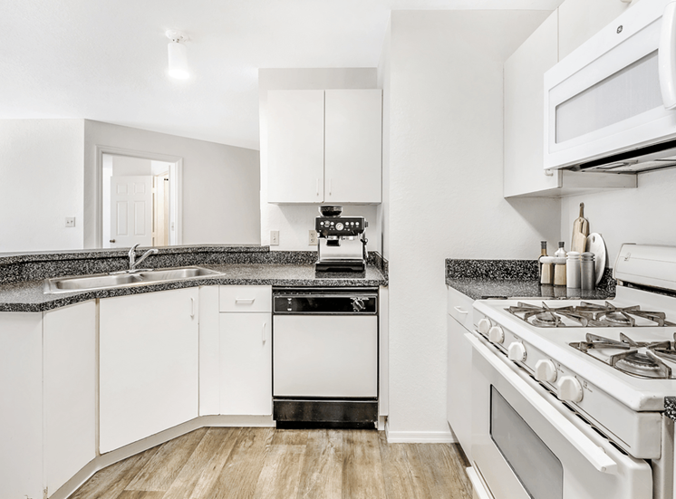 Virtually staged kitchen with white cabinets, gray countertop, white appliances, gas stove and wood flooring