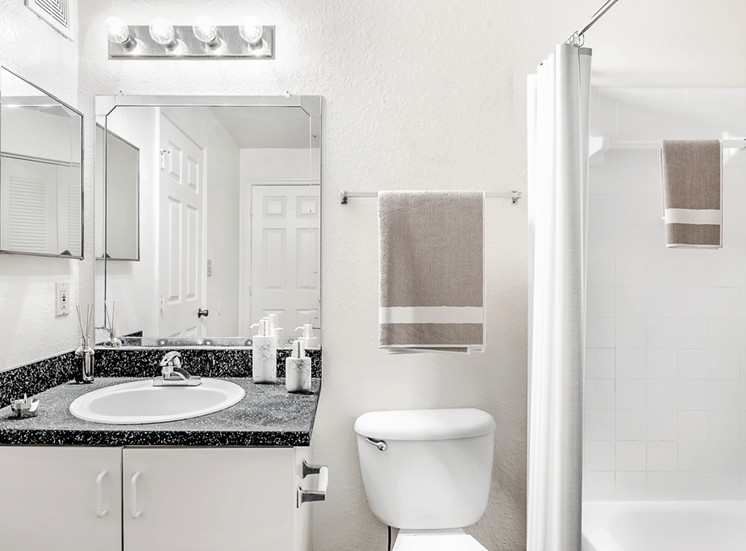 Virtually staged bathroom with large mirror, gray countertop, medicine cabinet, white cabinets and tiled tub with white shower curtain