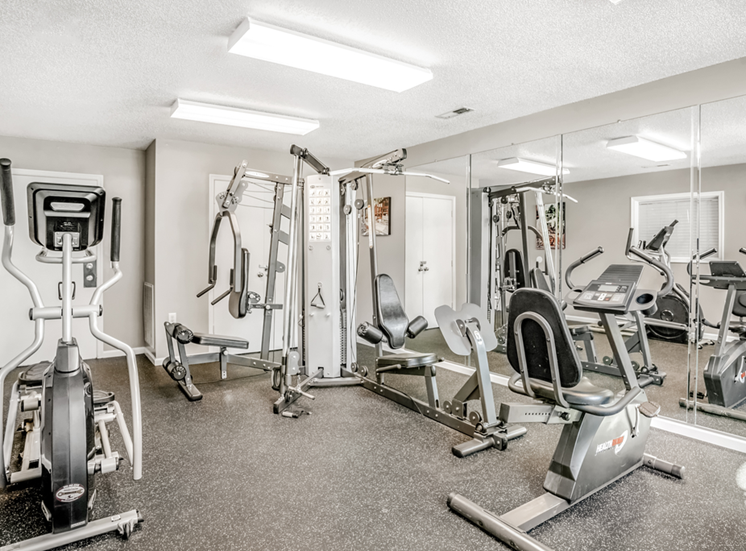 The community fitness center features several machines, including a chest press station, stationary bike, elliptical machine, and several cable exercise machines.
