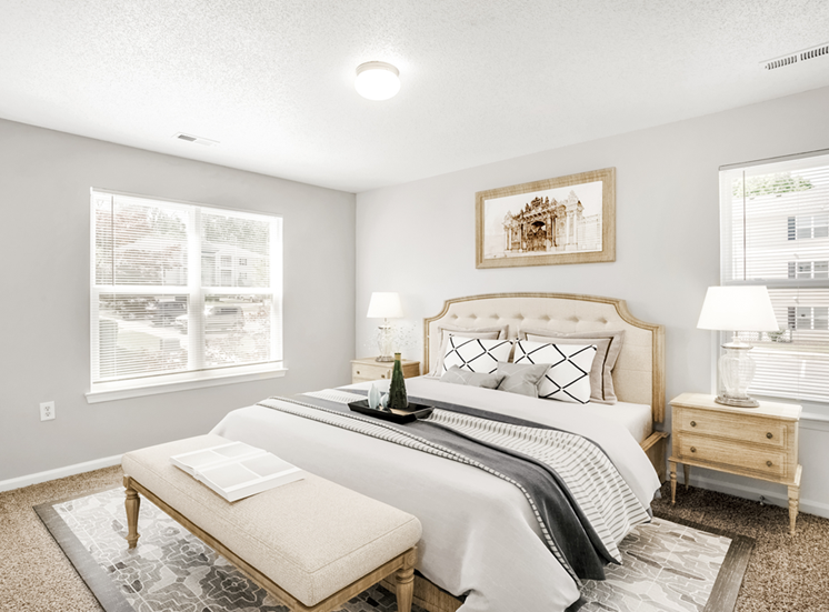 The vacant bedroom features tan carpet throughout with beige walls and a white textured ceiling. Windows are located on the right and left sides of the room providing ample natural light and feature blinds on both.