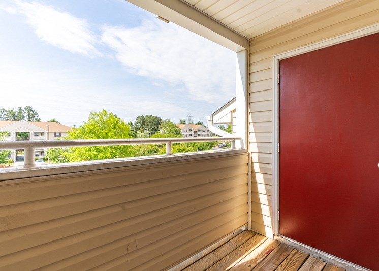 Balcony view with red storage door and view of trees in the background