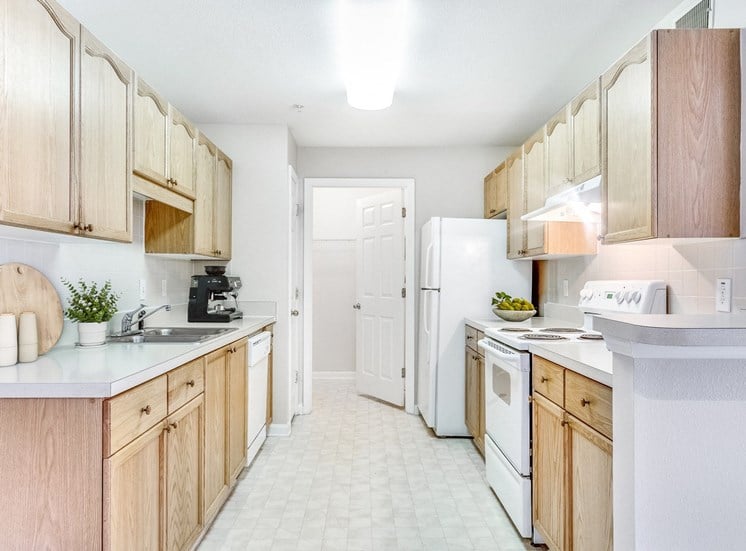 Staged  kitchen with white appliances, brown cabinets, and tile flooring.