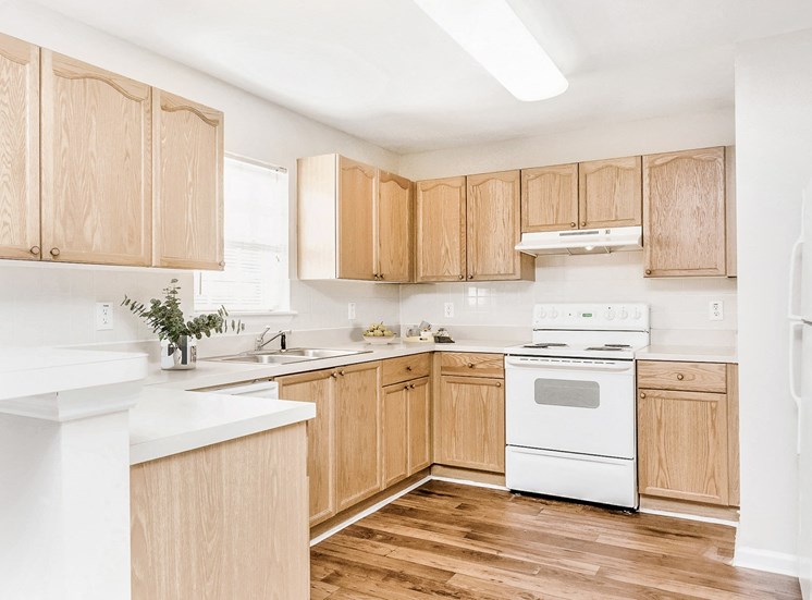 Staged vacant kitchen with white appliances, brown cabinets, and hardwood style flooring and décor on countertop.
