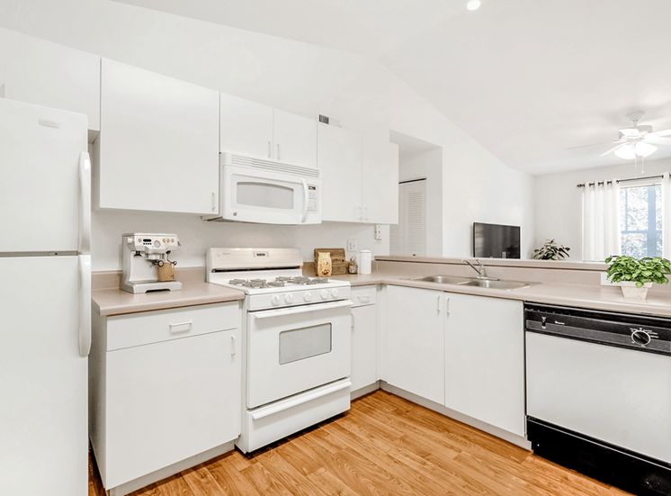 Virtually staged kitchen with white appliances, wood flooring, gas stove, ceiling fan, wall mounted television, dishwasher