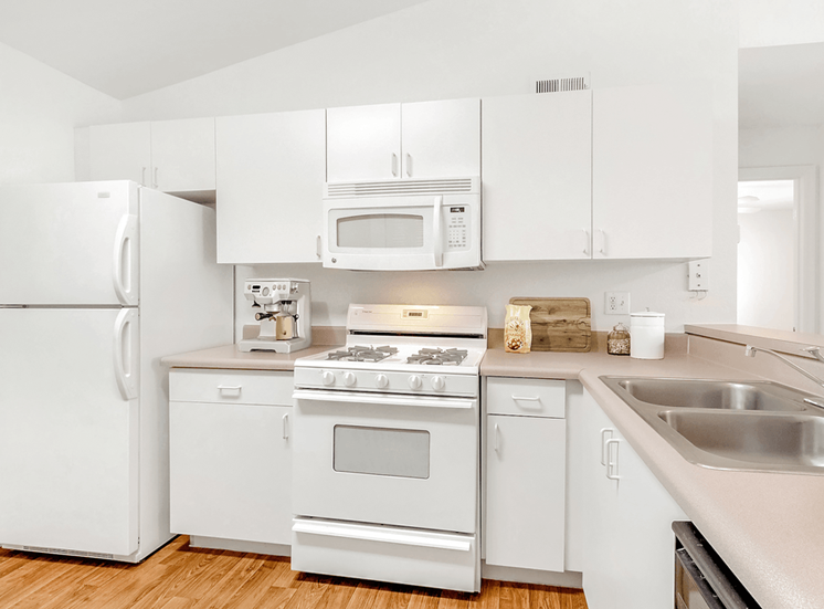 Virtually staged kitchen with white appliances, wood flooring, gas stove