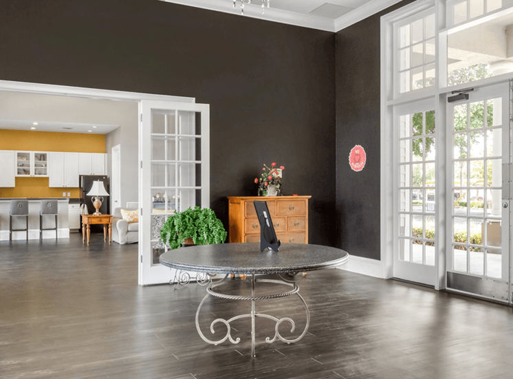 Clubhouse entryway with dark accent walls, wood style flooring, large windows and doors and kitchen in background