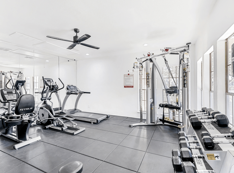 Fitness center with cardio and strength machines, dumb bell free weights, wall mirrors, ceiling fans and recessed lighting with many windows