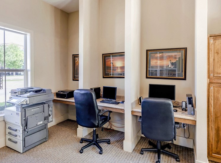 Business center with computers, rolling gray chairs, photos on the wall, light gray carpet, and a printer.