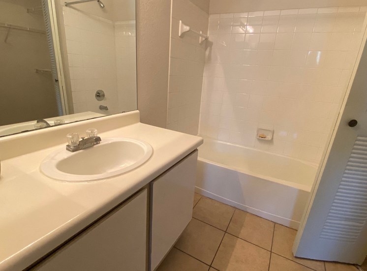 Bathroom with tile floors, toilet, shower tub combo with tile back splash, towel bar, white cabinets and view of closet