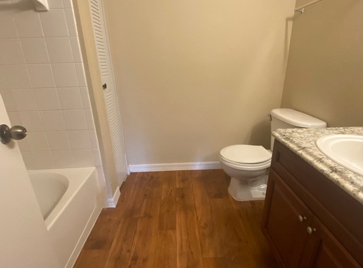 Bathroom with wood floors, granite vinyl  countertop, tub with tile back splash, and toilet
