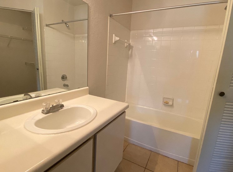 Bathroom with tile floors, toilet, shower tub combo with tile back splash, towel bar, white cabinets and large mirror