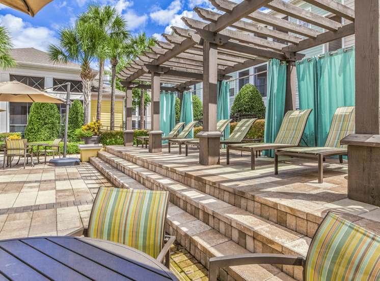 Poolside sundeck with lounge seating, shaded picnic tables, surrounded by palm trees
